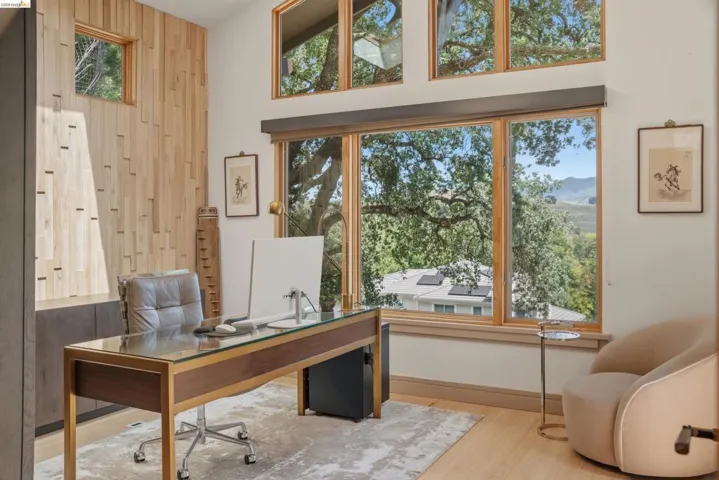 Vaulted ceiling with natural wood window frames, a wood-paneled accent wall, built-in cabinetry, and wood-finish flooring