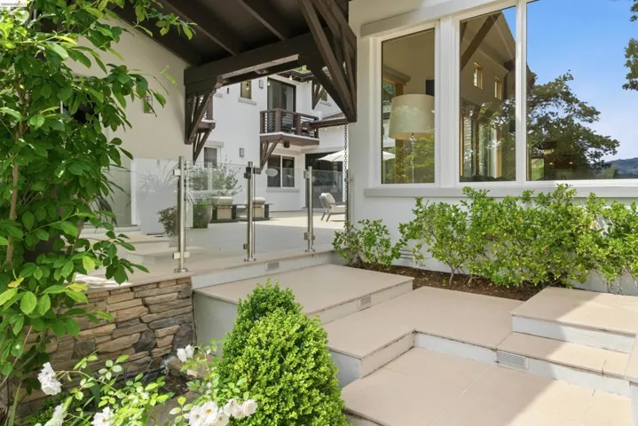 Exterior patio featuring stone steps, glass panel railing, and surrounding landscaping