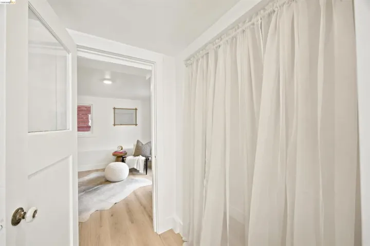 Crisp white walls and light wood-finish flooring characterize this room, accessible through a white paneled door with a porcelain knob