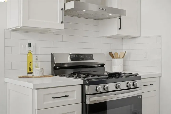 Stainless steel range with a gas cooktop, white subway tile backsplash, white shaker-style cabinetry, white countertops, and a stainless steel vent hood