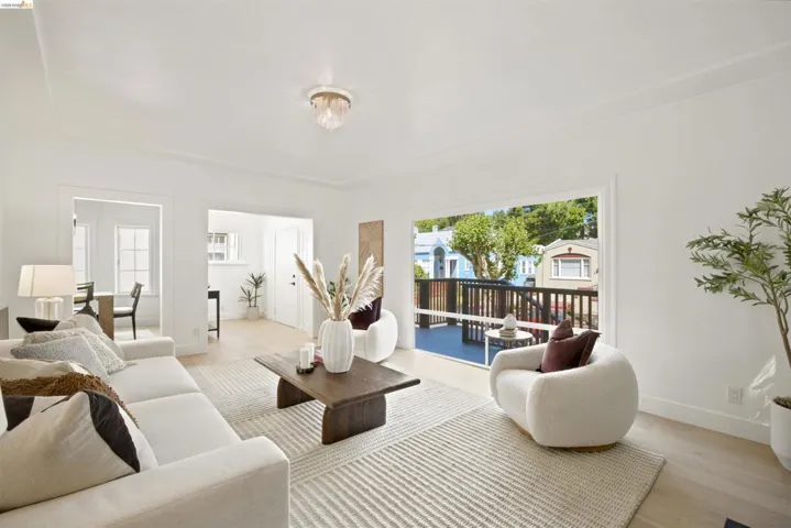 Living area featuring light wood-finish flooring, white walls, and a large picture window opening to an outdoor deck