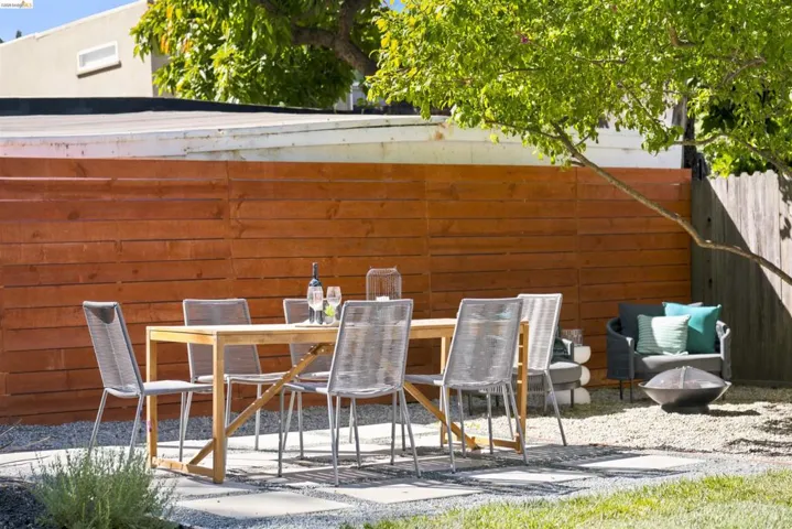 Outdoor dining area featuring a wood-finish fence, gravel ground cover, and a mature tree providing shade