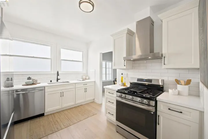 Modern kitchen featuring white shaker cabinetry, stainless steel appliances, light wood-finish flooring, white subway tile backsplash, and a wall-mounted range hood