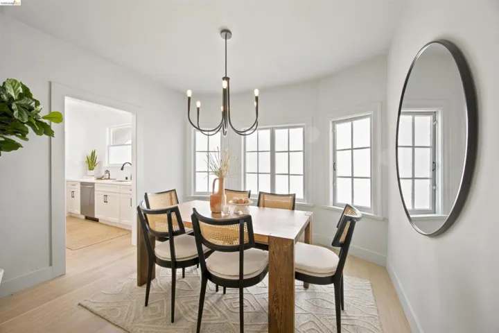 Dining area featuring light wood-finish flooring, a contemporary chandelier, a bay window with multiple panes, and a large round wall mirror
