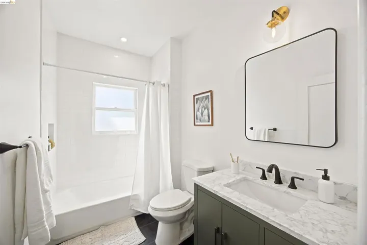 Bathroom featuring a dark green vanity with a marble-patterned countertop and undermount sink, matte black faucet, and a rectangular mirror with a black frame