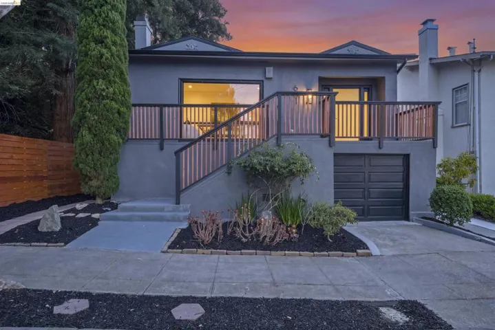 Stucco exterior featuring a wood fence, a mature evergreen tree, a black paneled garage door, and a front deck with a wood and metal railing