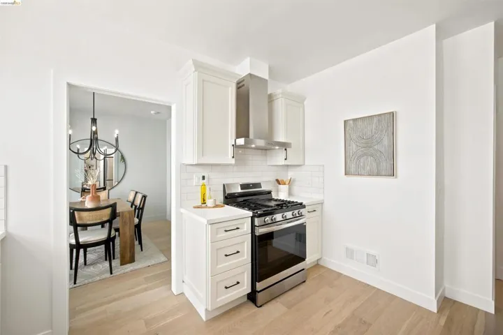 Kitchen area featuring light wood-finish flooring, white cabinetry, a stainless steel gas range, and a subway tile backsplash