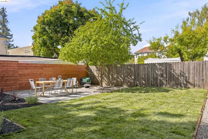 Expansive backyard featuring a lush lawn area, a paved patio with stepping stones, a modern horizontal wood fence, and mature trees providing natural shade
