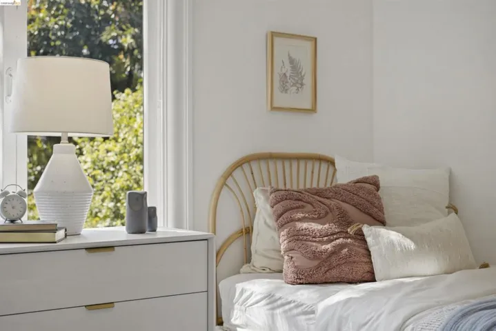 White room featuring a window with natural light, a light-colored dresser, a decorative table lamp, a woven headboard, and light wall finishes