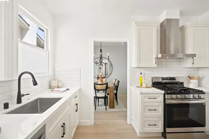 Contemporary kitchen featuring white cabinetry, quartz countertops, a matte black faucet, stainless steel appliances, and wood-finish flooring