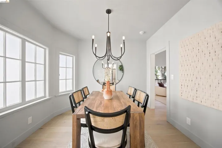 Dining area featuring light wood-finish flooring, a contemporary black chandelier, and bay windows with white trim