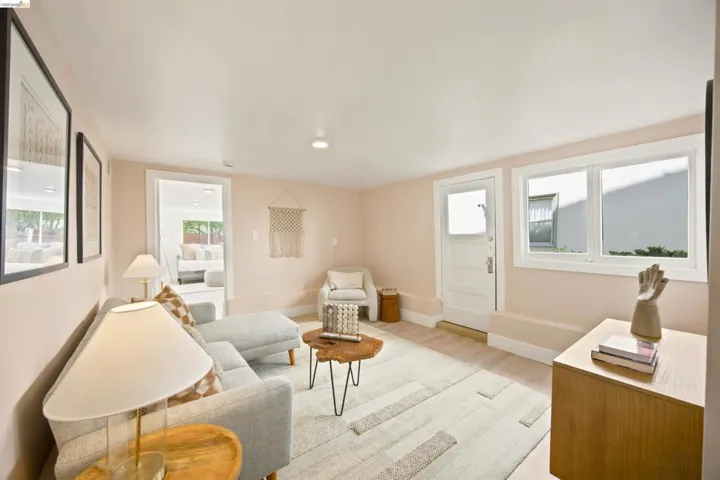 Spacious living area featuring light-toned walls, wood-finish flooring, white trim, a solid panel door with upper glass pane, and a doorway opening to an additional room