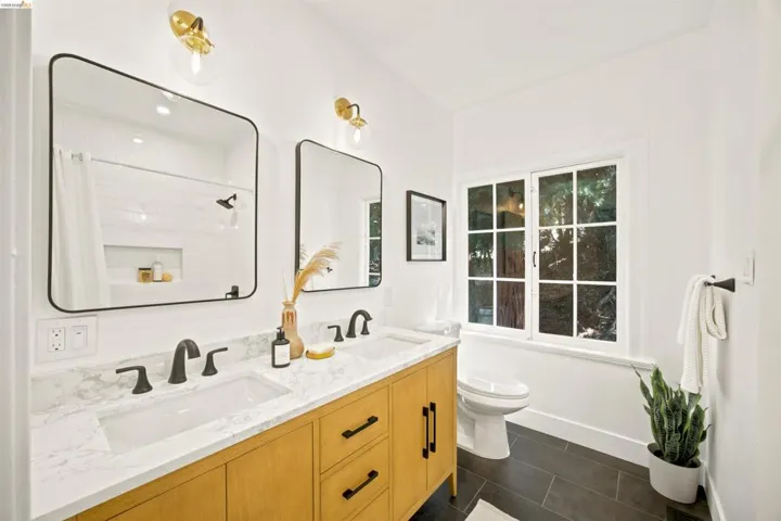 Double vanity with a stone countertop and integrated sinks, matte black fixtures, and gold-finish wall sconces