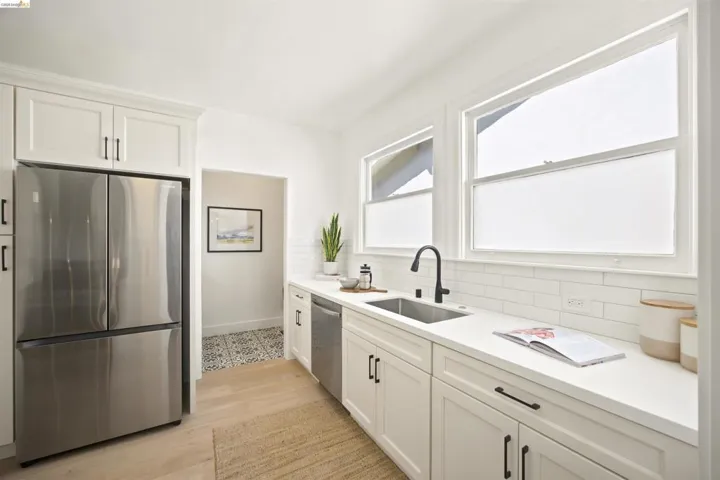 Modern kitchen featuring light wood-finish flooring, white shaker-style cabinetry with matte black hardware, and a stainless steel refrigerator
