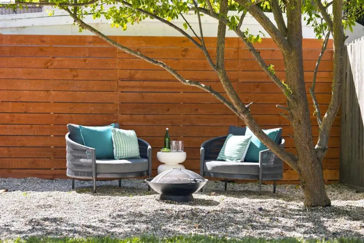 Gravel patio area featuring a horizontal plank privacy fence and mature tree
