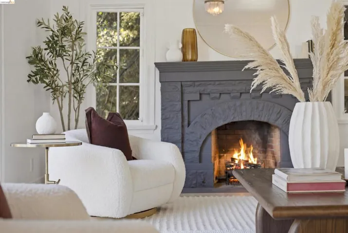 Living room featuring a dark gray stone fireplace with an arched opening, a white window with multiple panes, and light-toned walls