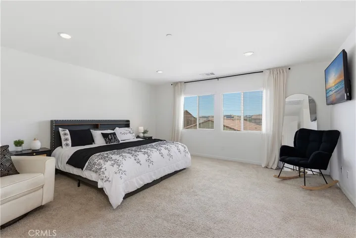 Primary suite features large picture windows with black curtain rods and linen drapes, complemented by recessed lighting for a bright, serene retreat.