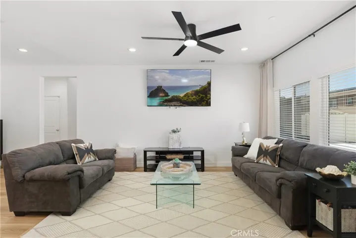 Sun-filled great room featuring wide-plank natural tone laminate flooring, sleek black modern fan, and oversized picture windows that create a light, airy feel, complemented by black curtain rods and linen drapery