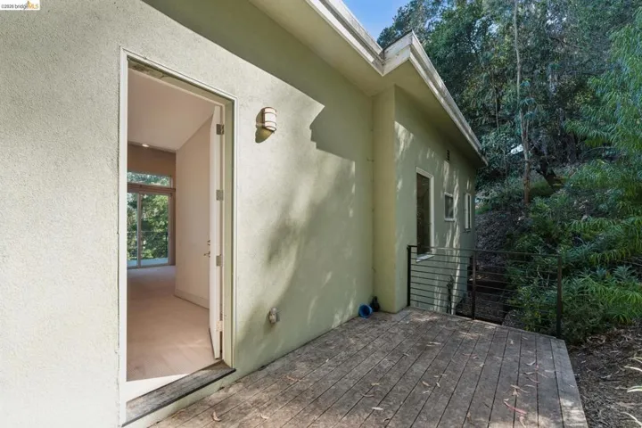 Outdoor wooden deck with a stucco exterior, integrated wall sconce, and black horizontal railing