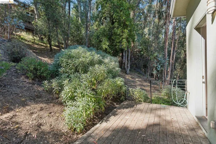 Exterior deck featuring wood-finish flooring, metal railing, and direct access to a natural landscape with mature trees and varied foliage