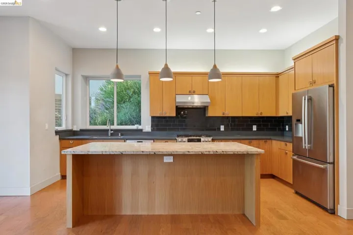 Kitchen featuring a central island with a light-toned countertop, wood-finish cabinetry, stainless steel appliances, dark subway tile backsplash, and recessed lighting