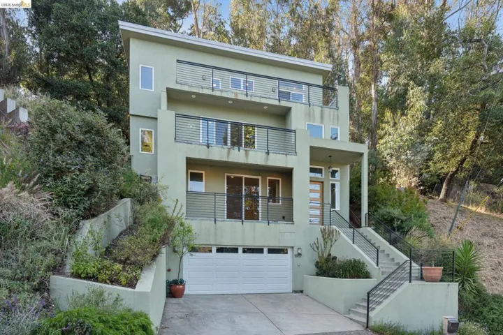 Contemporary three-story residence featuring a two-car garage, multiple balconies with horizontal railings, and a prominent wood-panelled entry​​‌​​​​‌​​‌‌​​‌​​​‌‌​​​‌​​‌‌​​‌‌​​‌‌​​​​ door