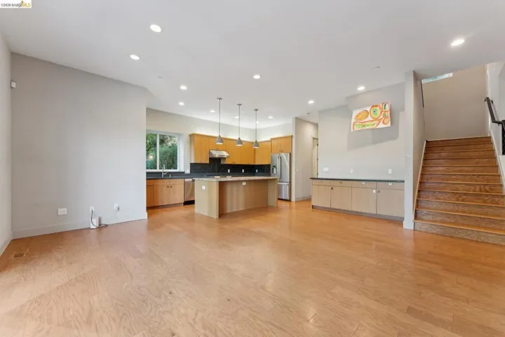 Open-concept floor plan featuring light wood-finish flooring, a modern kitchen with natural wood cabinetry and a central island, stainless steel appliances, and recessed lighting