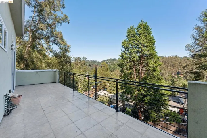 Expansive outdoor deck with square tile flooring, featuring horizontal metal railings and surrounding mature trees