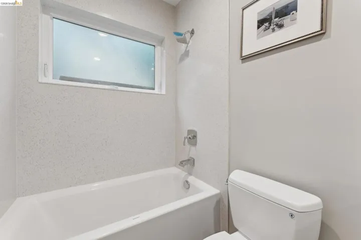 White bathtub with a chrome shower fixture, surrounded by light-toned, textured wall panels