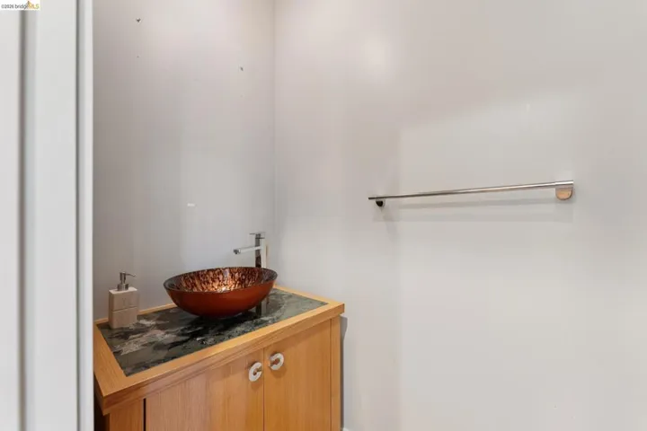 Modern vanity featuring a vessel sink with a contemporary faucet, wood cabinetry, and a stone-finish countertop