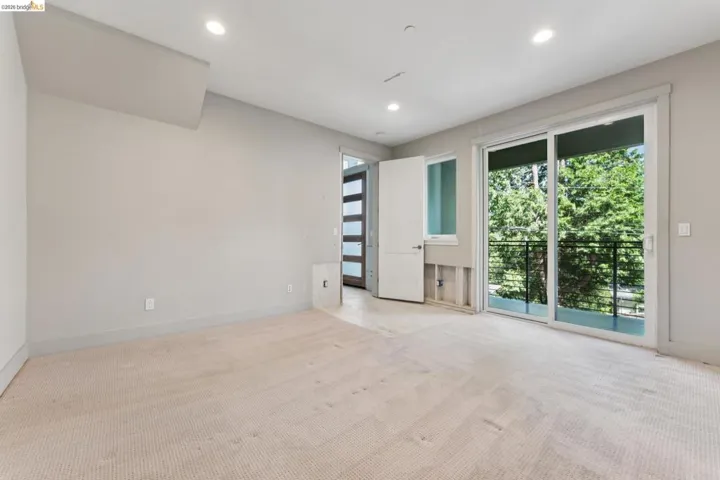 Spacious room featuring light-colored carpeting, recessed lighting, and a full-light glass sliding door