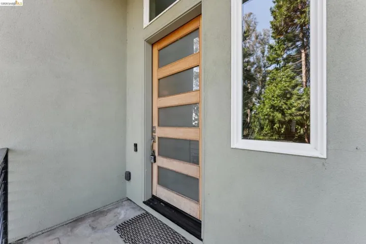 Modern wood-paneled entry door with frosted glass inserts, complemented by a transom window and a side window with white trim, set against a light stucco exterior