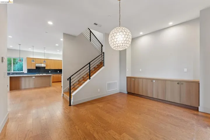 Open-concept living area with wood-finish flooring, a contemporary staircase featuring black railings, and a honeycomb-patterned pendant light fixture