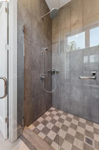 Walk-in shower featuring full-height grey wall tiling, a rainfall showerhead, and a handheld shower fixture