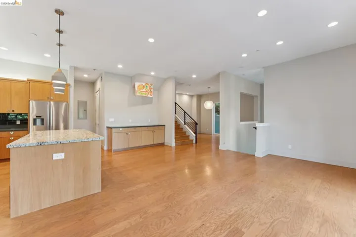 Open-concept living space featuring wood-finish flooring, recessed lighting, and a kitchen island with a light-toned stone countertop