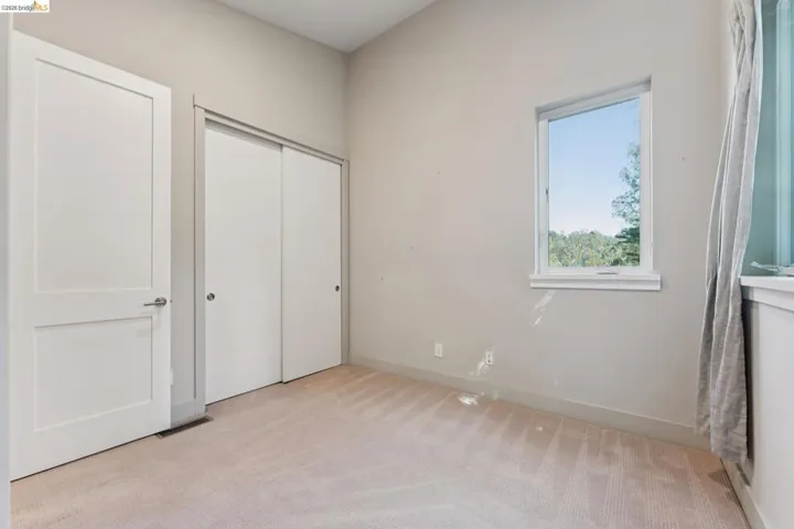 Neutral-toned room featuring a single window with white trim, light beige carpeting, a white interior door with brushed nickel hardware, and a white sliding closet door