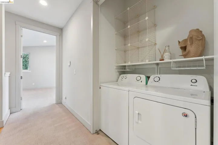 Dedicated laundry area featuring white appliances, a white wall shelf, and overhead wire shelving