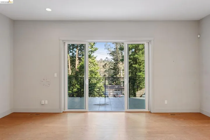 Expansive sliding glass doors opening to an outdoor balcony with black metal railing, offering tree-filled scenery