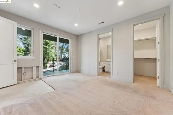 Spacious room featuring a glass sliding door to a balcony, an additional window, recessed lighting, and a private bath with a vanity and mirror