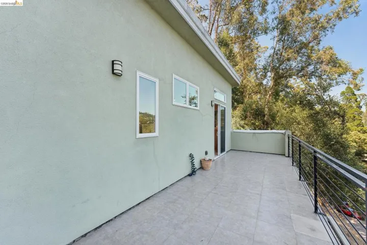 Expansive outdoor terrace featuring gray tile flooring, a contemporary black metal railing, and a light green stucco exterior