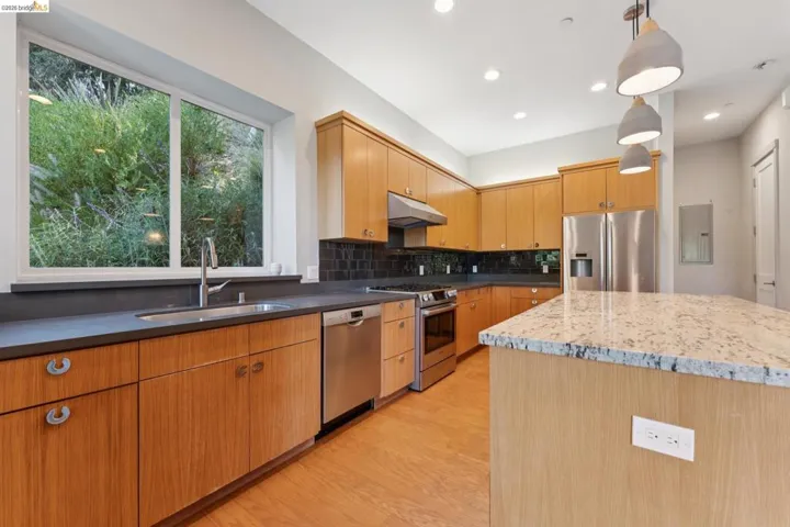 Kitchen featuring wood-finish cabinetry, stainless steel appliances, dark countertops, a tile backsplash, and a central island with a light-toned, speckled countertop