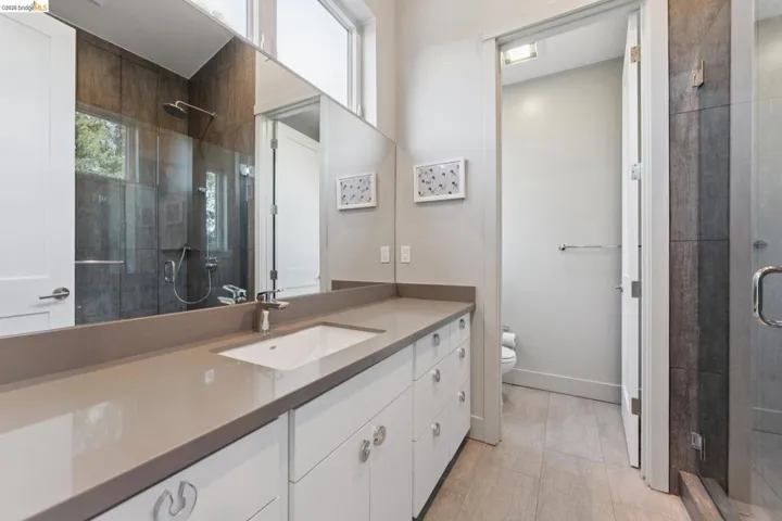 Spacious bathroom featuring a double vanity with an integrated sink, a large mirror, and a glass-enclosed shower with a rainfall showerhead