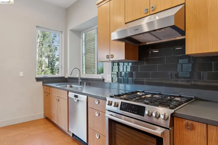 Kitchen featuring natural wood cabinetry, stainless steel appliances, dark subway tile backsplash, and composite countertops