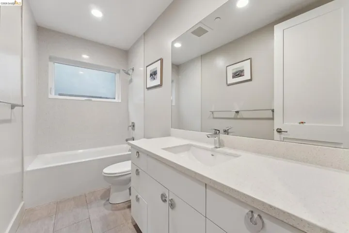 Contemporary bathroom featuring a spacious white vanity with an integrated sink, a large mirror, and recessed lighting