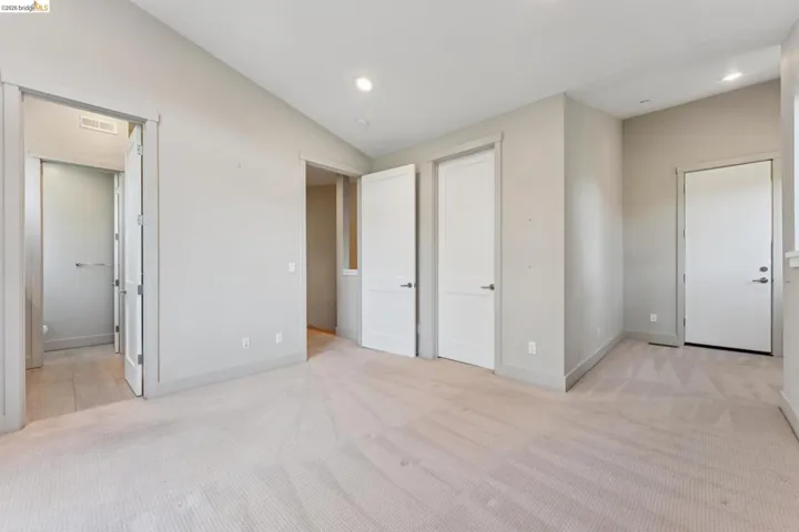 Spacious room featuring light-toned carpet, neutral wall finishes, and multiple white panel doors with contemporary hardware