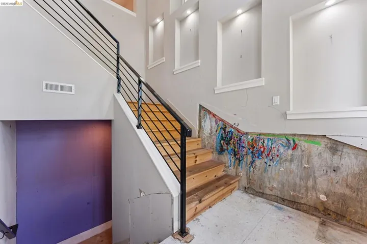 Two-story interior featuring a wood staircase with black metal railings, recessed wall niches with accent lighting, and a purple accent wall