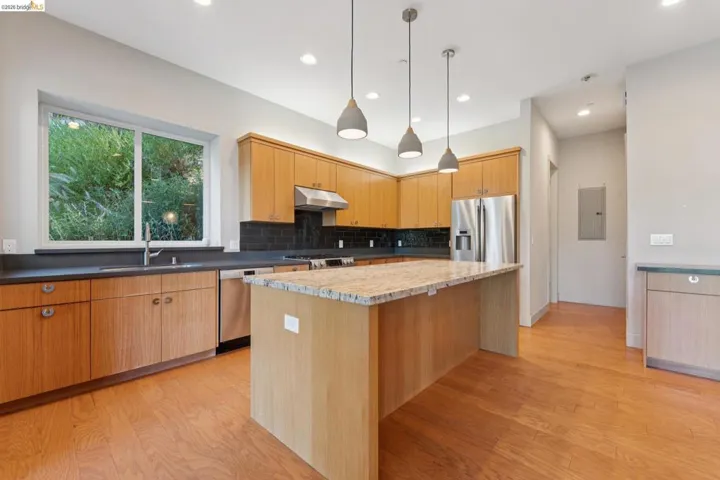 Kitchen featuring light wood cabinetry, a granite-topped island, stainless steel appliances, dark countertops, and wood-finish flooring