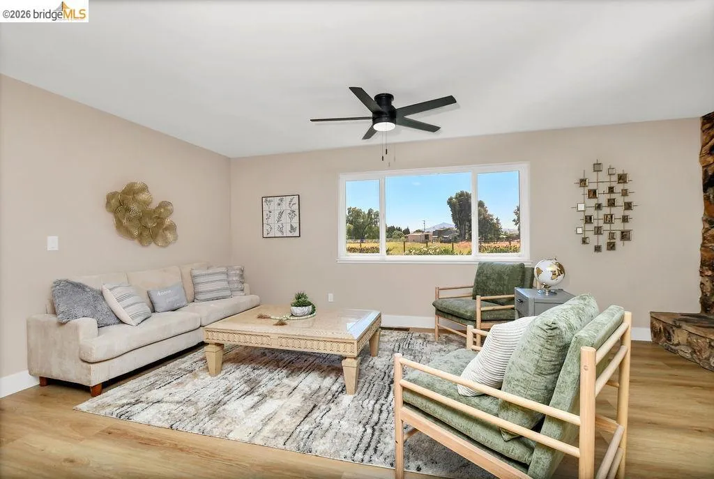 Living space featuring wood-finish flooring, a contemporary ceiling fan, and a large multi-pane window