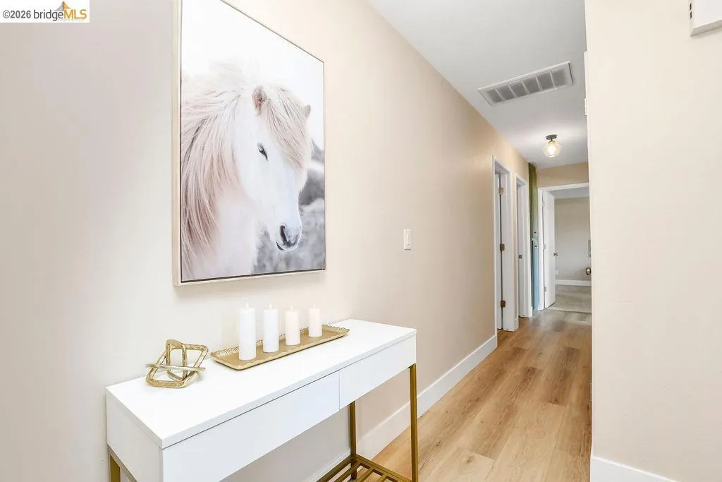 Hallway featuring wood-finish flooring, light tan wall paint, and white baseboards