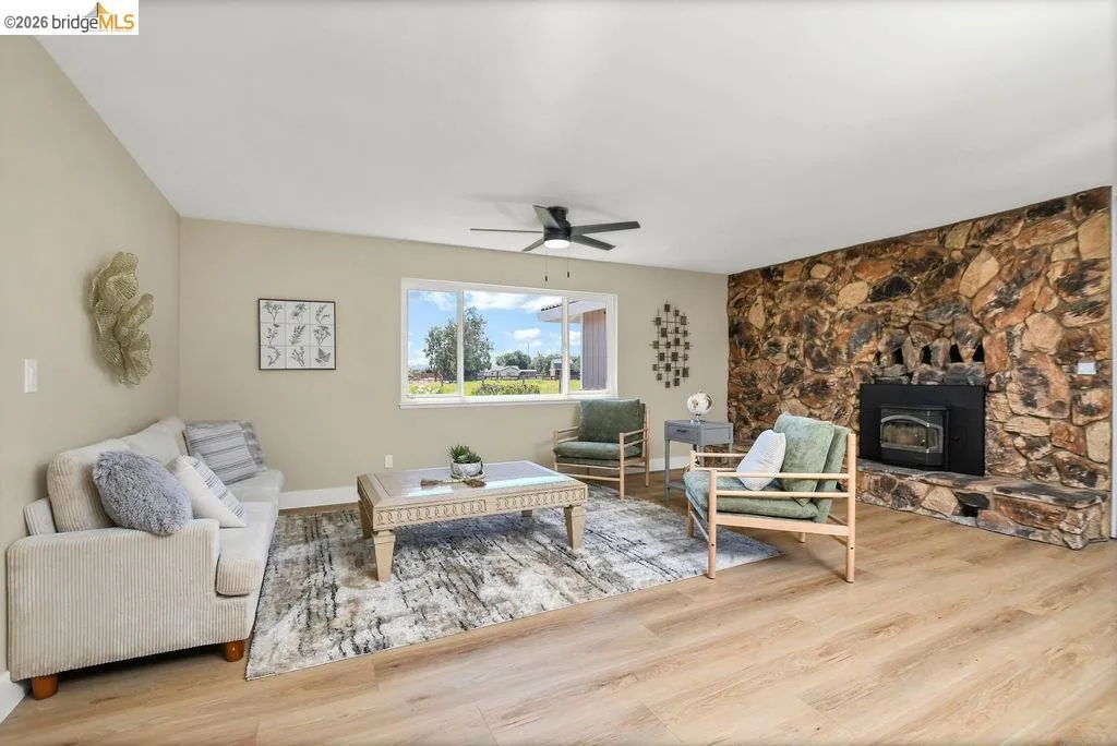 Spacious living area featuring a prominent stone-clad fireplace with a black insert, wood-finish flooring, and a ceiling fan